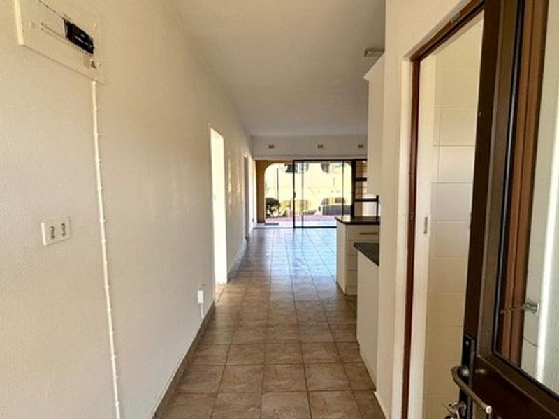 A view through a tiled hallway leading towards an open-plan living area with a sliding glass door providing access to the exterior.