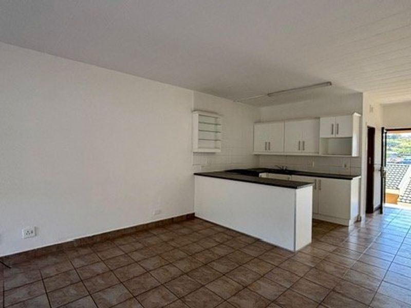 Open-plan living and kitchen area featuring tiled flooring, white cabinetry, and a breakfast island, leading to an exterior balcony.