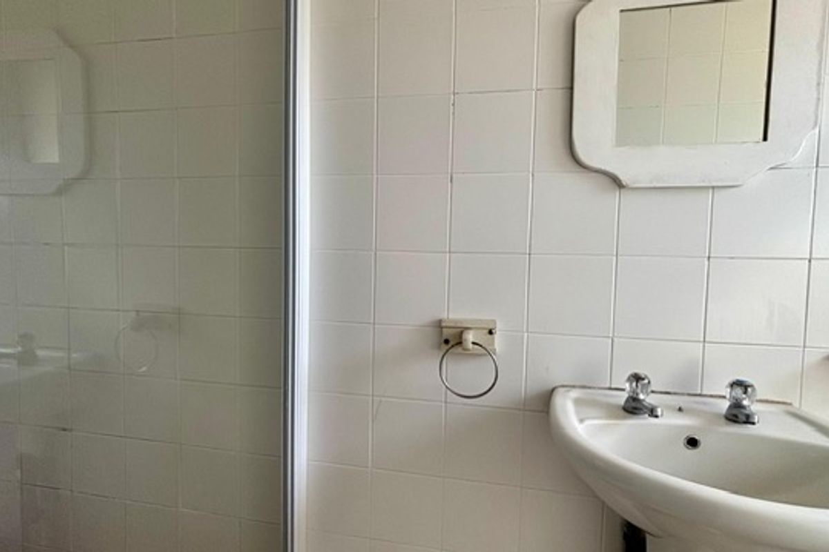 A dated bathroom featuring a pedestal basin, shower enclosure, and white ceramic wall tiles, requiring modernization to improve its aesthetic appeal.