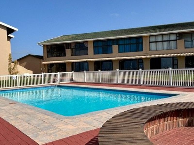 A well-maintained communal swimming pool area featuring paved surrounds, a white picket fence, and integrated brick seating, set against an apartment building facade.