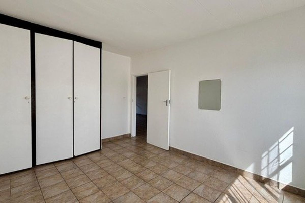 A clean, empty bedroom featuring neutral tiled flooring and built-in storage cupboards, offering a blank canvas for personalization.
