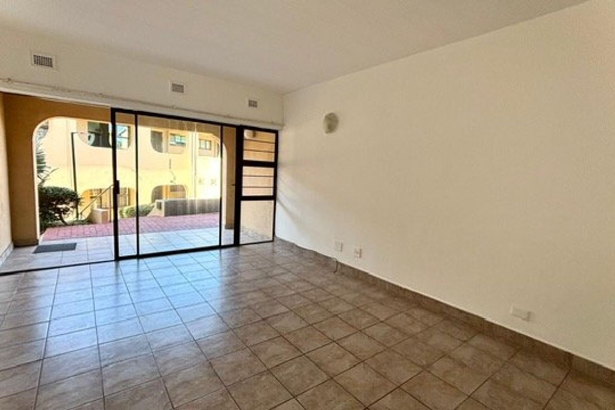 An empty living room featuring tiled flooring and a large sliding glass door providing access to an outdoor patio area.
