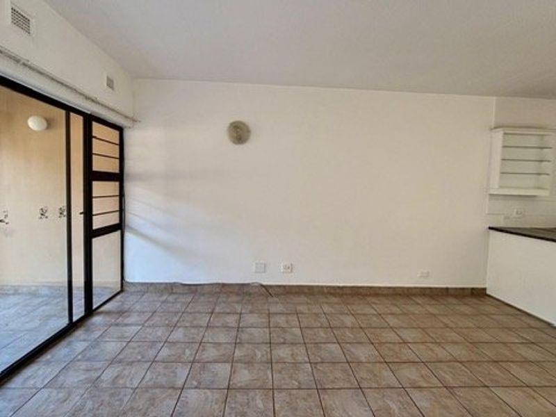 Spacious open-plan living area featuring tiled flooring, a large sliding glass door leading to the patio, and a functional kitchen counter area.