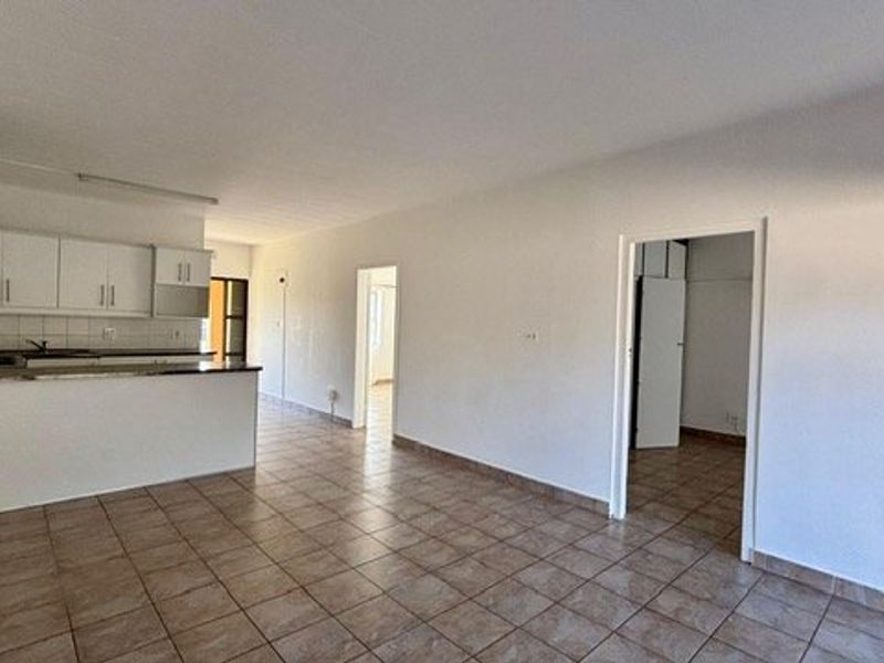 An open-plan living and kitchen area featuring tiled flooring, white cabinetry, and neutral walls, offering a blank canvas for interior design.