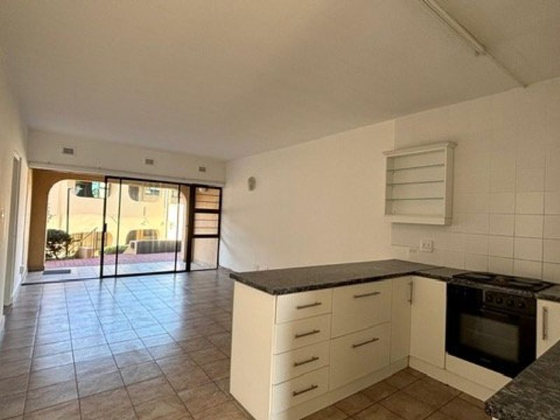 Open-plan living and kitchen area featuring tiled flooring, built-in cabinetry with oven and hob, and sliding glass doors leading to an outdoor space.