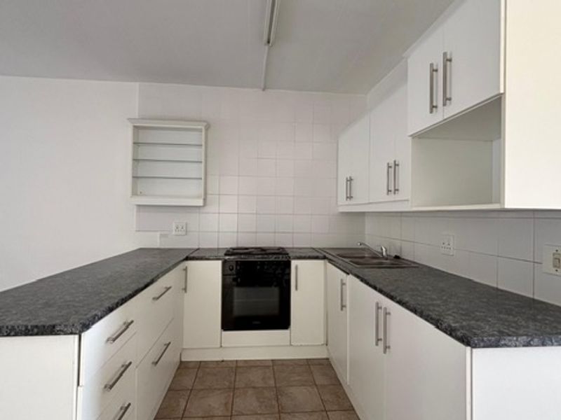 A clean, functional kitchen featuring white cabinetry, dark laminate countertops, a built-in oven, and a tiled backsplash.