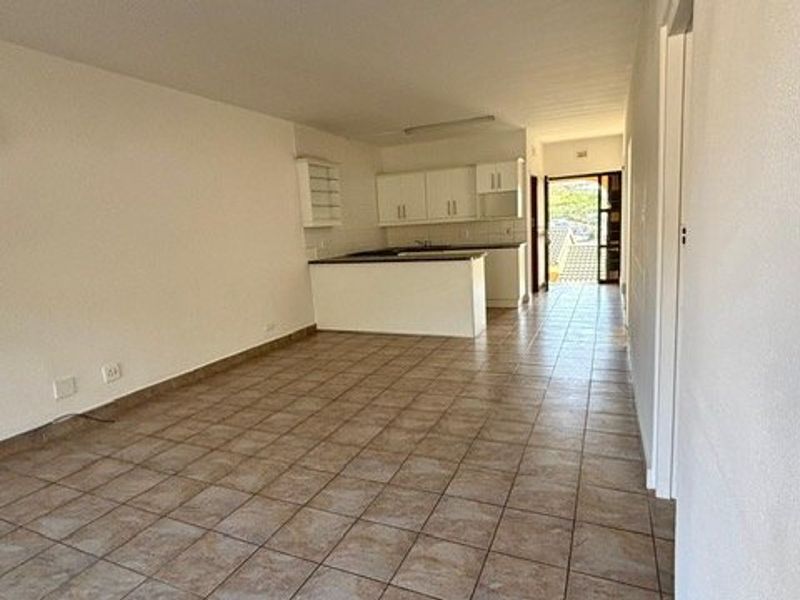 An open-plan living and kitchen area featuring tiled flooring, neutral walls, and basic kitchen cabinetry, offering a blank canvas for renovation.