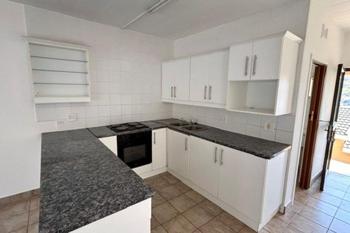 A clean, functional kitchen featuring white cabinetry, dark laminate countertops, built-in oven and hob, and tiled flooring with direct access to an outdoor area.
