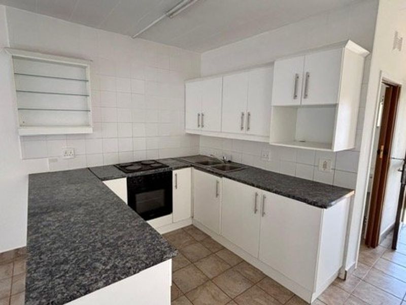 A clean, functional kitchen featuring white cabinetry, dark laminate countertops, built-in oven and hob, and tiled flooring with direct access to an outdoor area.