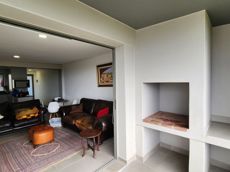 Covered balcony featuring a built-in braai and tiled flooring, seamlessly connecting to the open-plan living area through large sliding glass doors.