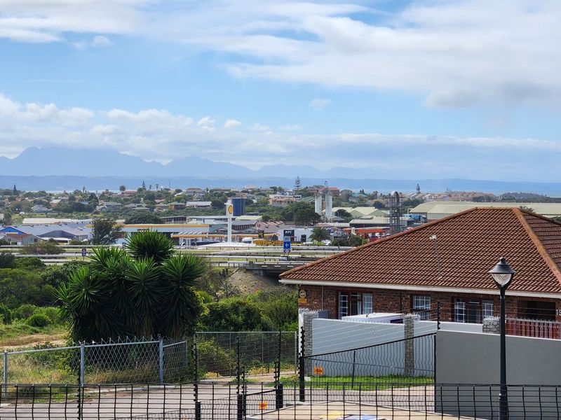 Elevated view overlooking the surrounding neighbourhood, industrial area, and distant mountain range, featuring a foreground view of a residential property with tiled roofing.
