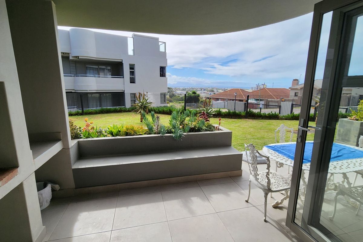 Covered patio featuring a built-in braai, tiled flooring, and a built-in concrete bench, overlooking a private garden area with scenic views.