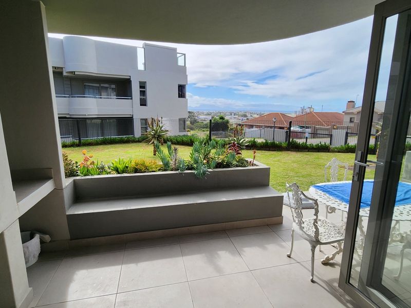 Covered patio featuring a built-in braai, tiled flooring, and a built-in concrete bench, overlooking a private garden area with scenic views.
