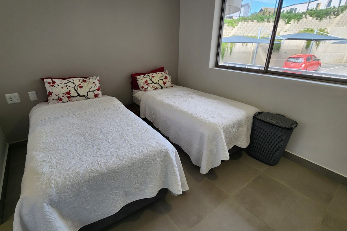 A functional bedroom featuring neutral wall tones, tiled flooring, and a large window providing natural light and exterior views.