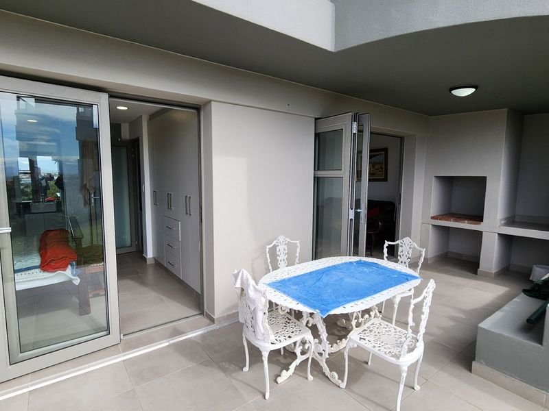 Spacious covered balcony featuring tiled flooring, built-in braai, and direct access to the interior through large aluminium sliding doors.