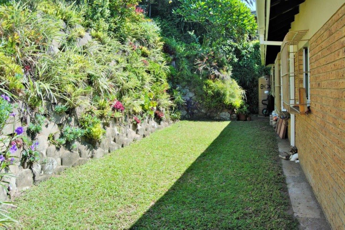 A well-maintained rear garden featuring a landscaped retaining wall, lawn area, and a water tank situated alongside the brick exterior of the house.