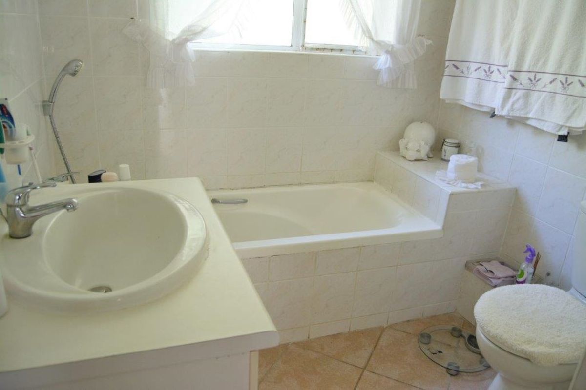 A functional bathroom featuring a built-in bathtub, vanity basin, and tiled finishes throughout, offering a clean and practical layout.