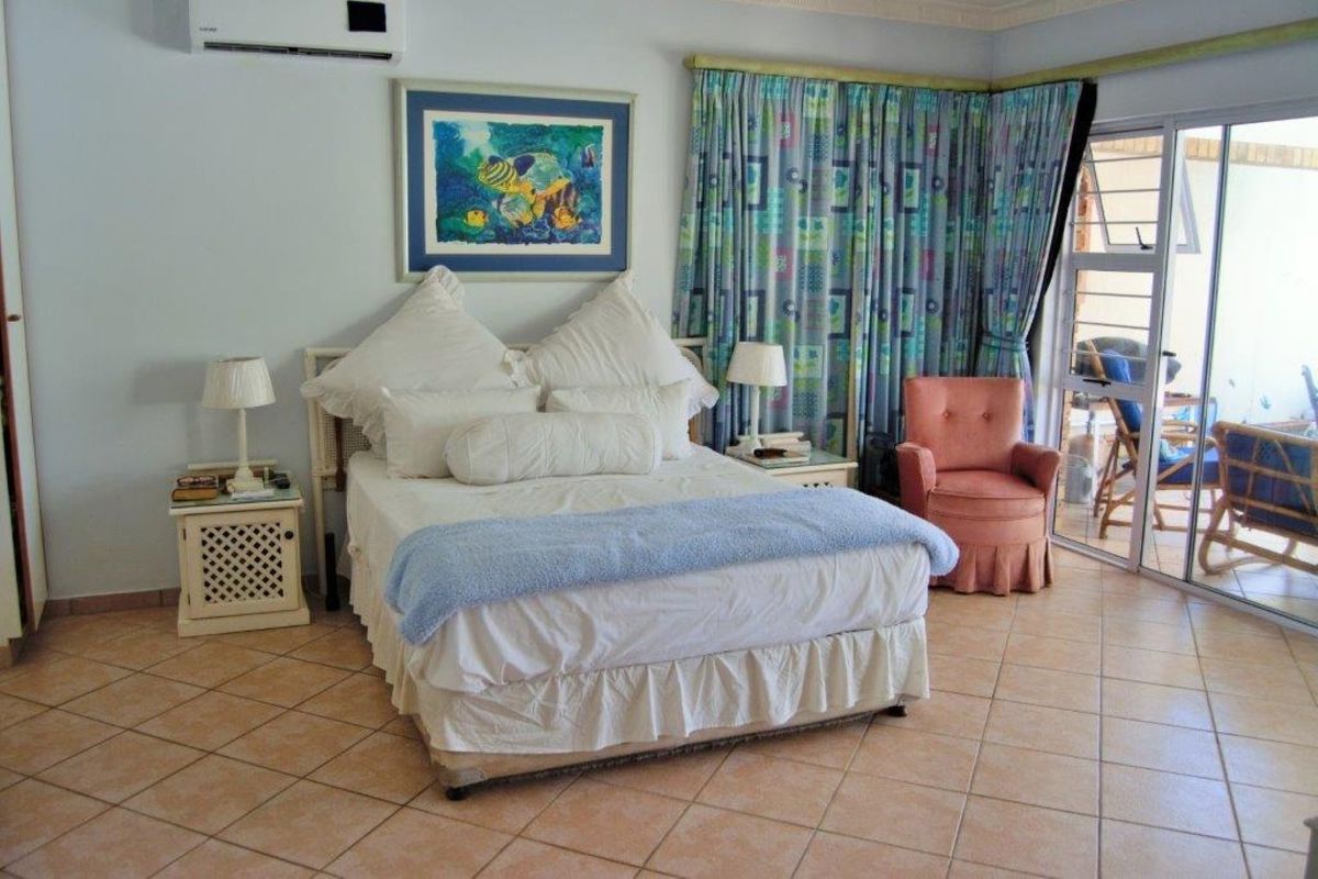Spacious bedroom featuring tiled flooring, a wall-mounted air conditioning unit, and direct access to an outdoor patio through sliding glass doors.