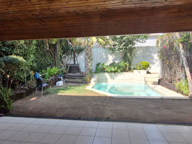 Outdoor entertainment area featuring a covered patio with timber ceiling overlooking a swimming pool and garden space.