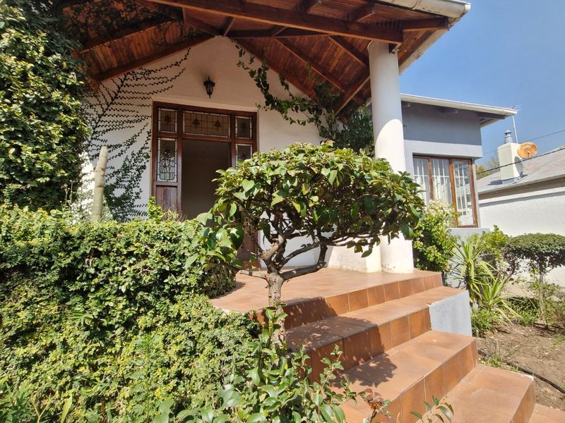Front entrance featuring a covered porch with timber roof structure, tiled steps, and a decorative leaded glass front door, surrounded by established garden greenery.