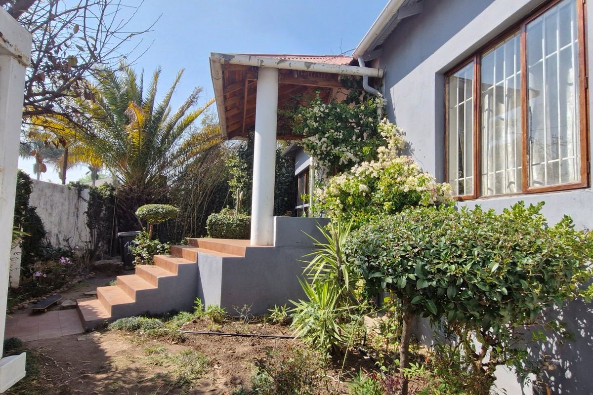 Rear exterior view of the house featuring a covered patio area, concrete steps, and established garden landscaping.