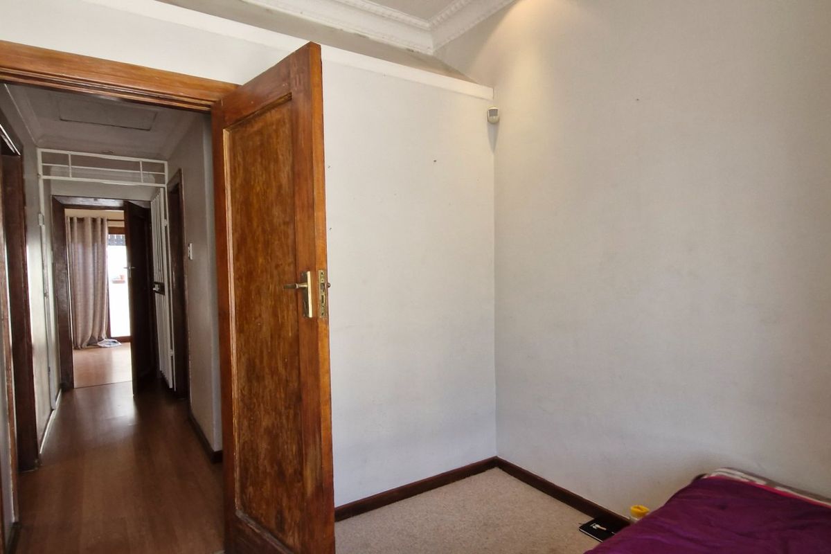 A bedroom interior featuring wooden door frames and ceiling cornices, showing signs of wear on the walls and door finishes.