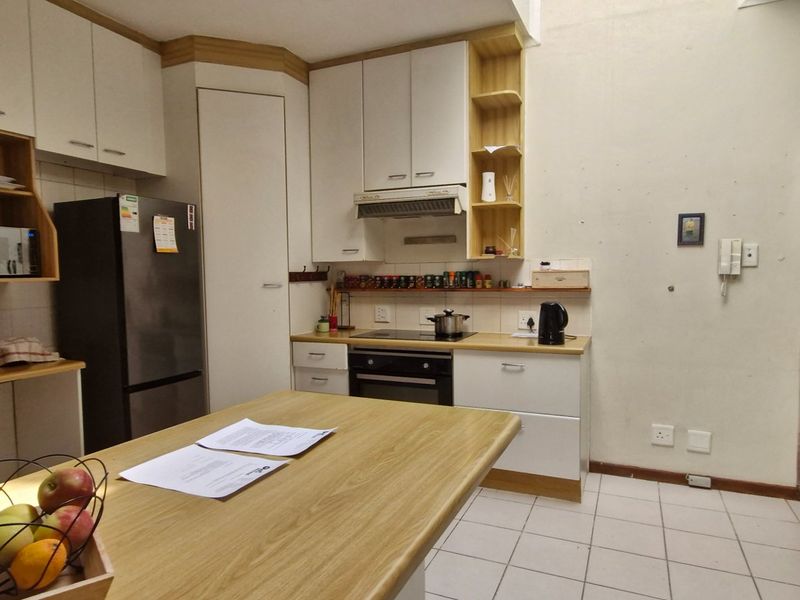 A functional kitchen featuring white cabinetry, laminate countertops, built-in oven and hob, and tiled flooring, with an open-plan layout leading to the living area.