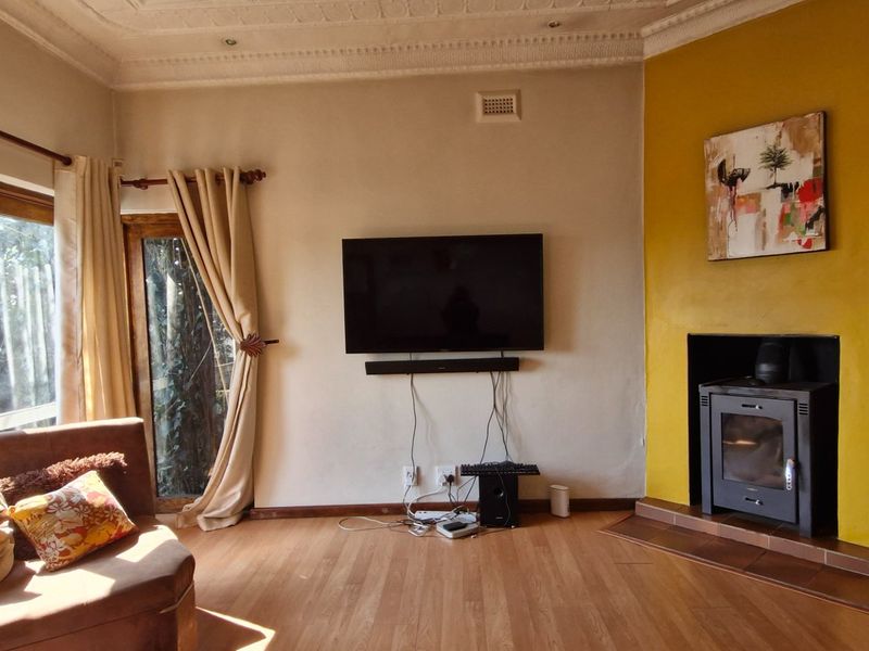 A cozy living room featuring a wood-burning fireplace, laminate flooring, and decorative ceiling cornices, with large windows providing natural light.