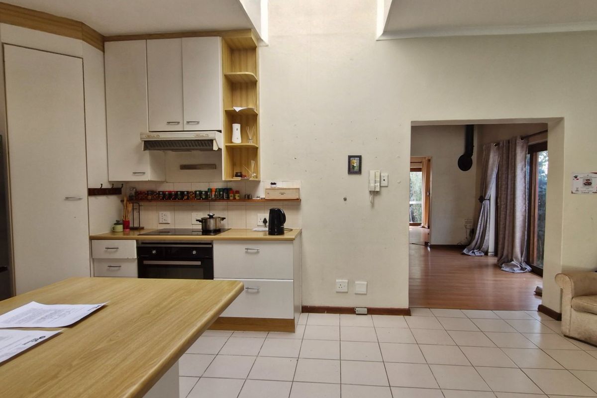 A functional kitchen featuring built-in cabinetry, an electric oven and hob, and a central island, with tiled flooring and direct access to the living area.