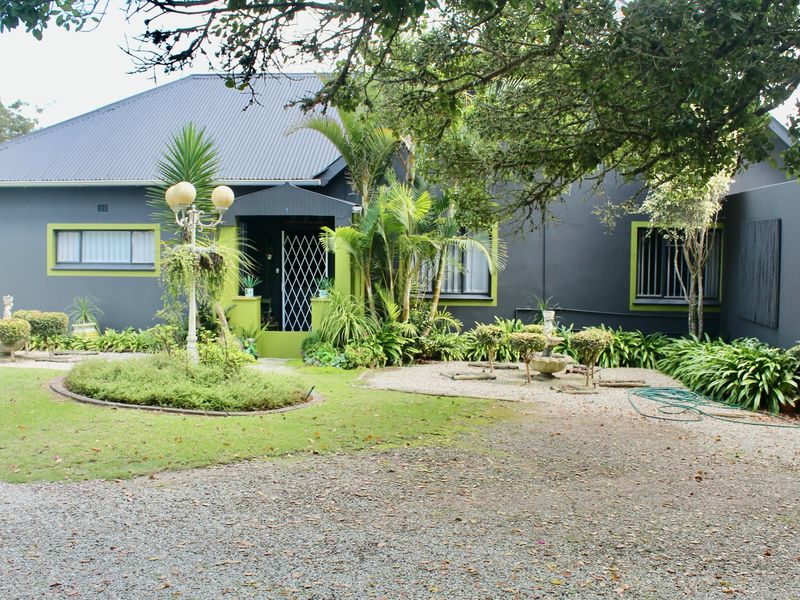 Front elevation of a farm-style residence featuring a dark grey facade with lime green accents, a corrugated metal roof, and a gravel driveway.