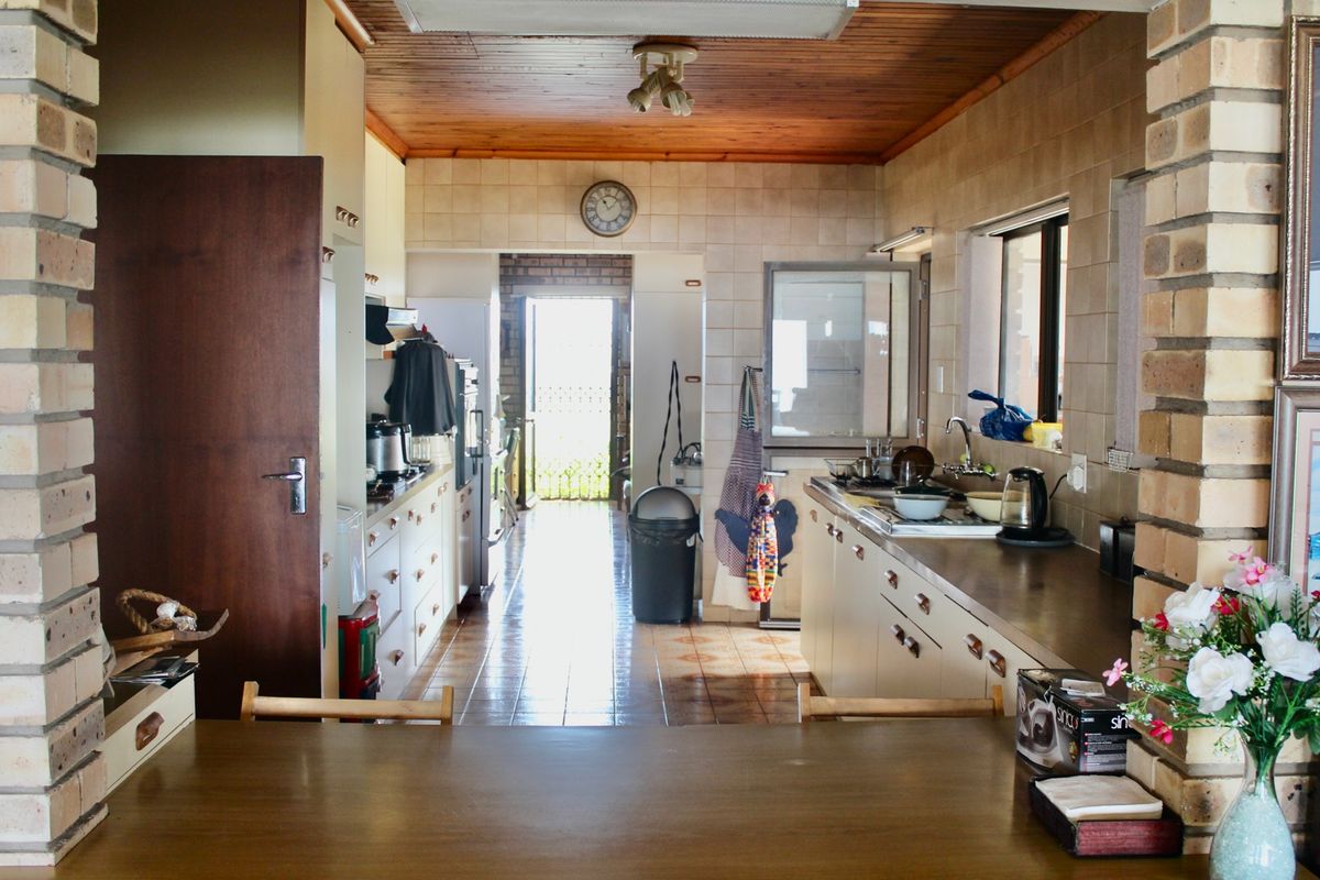 A functional kitchen featuring timber ceilings, exposed brick accents, tiled countertops, and ample built-in cabinetry, leading through to an exterior access point.