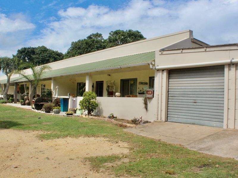Front elevation of a farm-style property featuring a long covered patio, double garage with roll-up doors, and a surrounding lawn area.