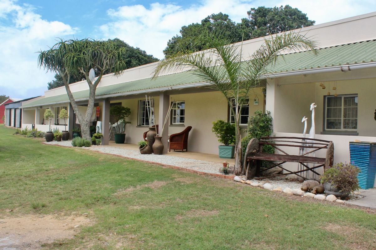 A well-maintained rear exterior view of the farm dwelling featuring a long covered patio, concrete pillars, and a green corrugated metal roof.
