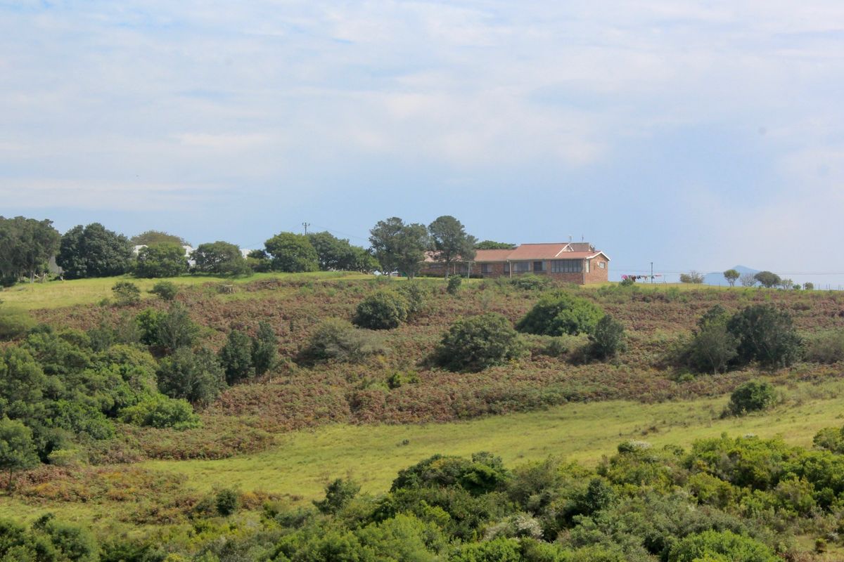 An elevated view of a farmhouse situated on a large, grassy rural property with surrounding trees and natural landscape.