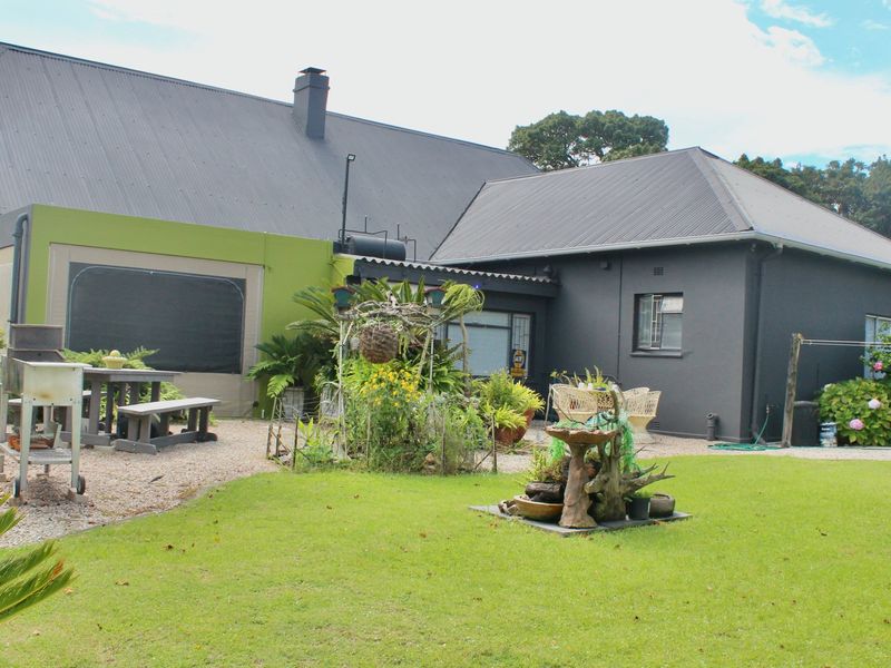 Rear view of the farmhouse featuring a dark-painted exterior, corrugated metal roofing, a gravel patio area, and a well-maintained lawn.