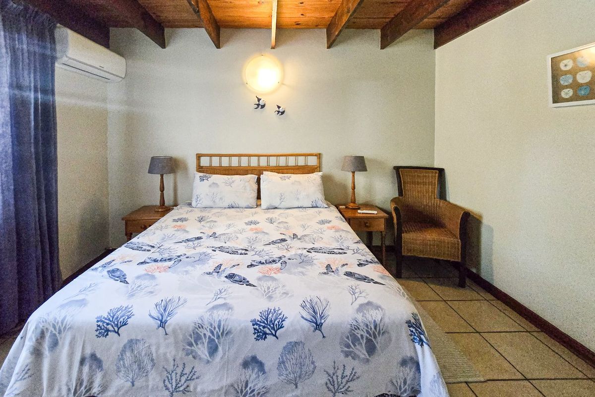 A bedroom featuring exposed timber ceiling beams, tiled flooring, and a wall-mounted air conditioning unit.