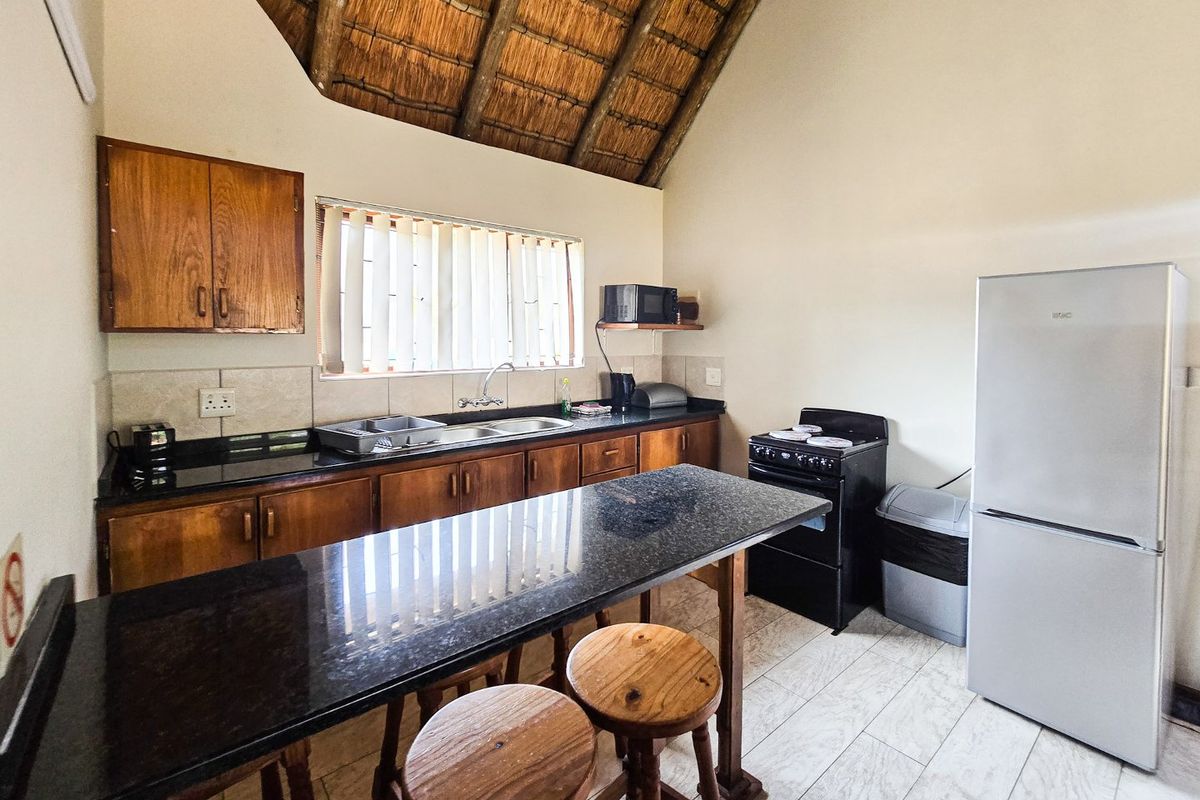A functional kitchen featuring granite countertops, wooden cabinetry, and a distinctive high-pitched thatched roof ceiling, providing a rustic aesthetic.