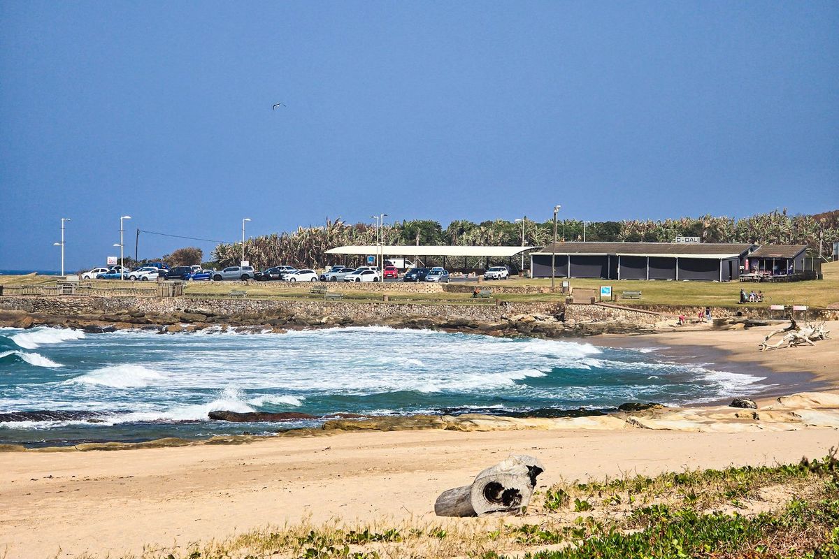A scenic view of a coastal commercial property featuring a stone retaining wall, paved parking area, and a covered structure overlooking the beach.
