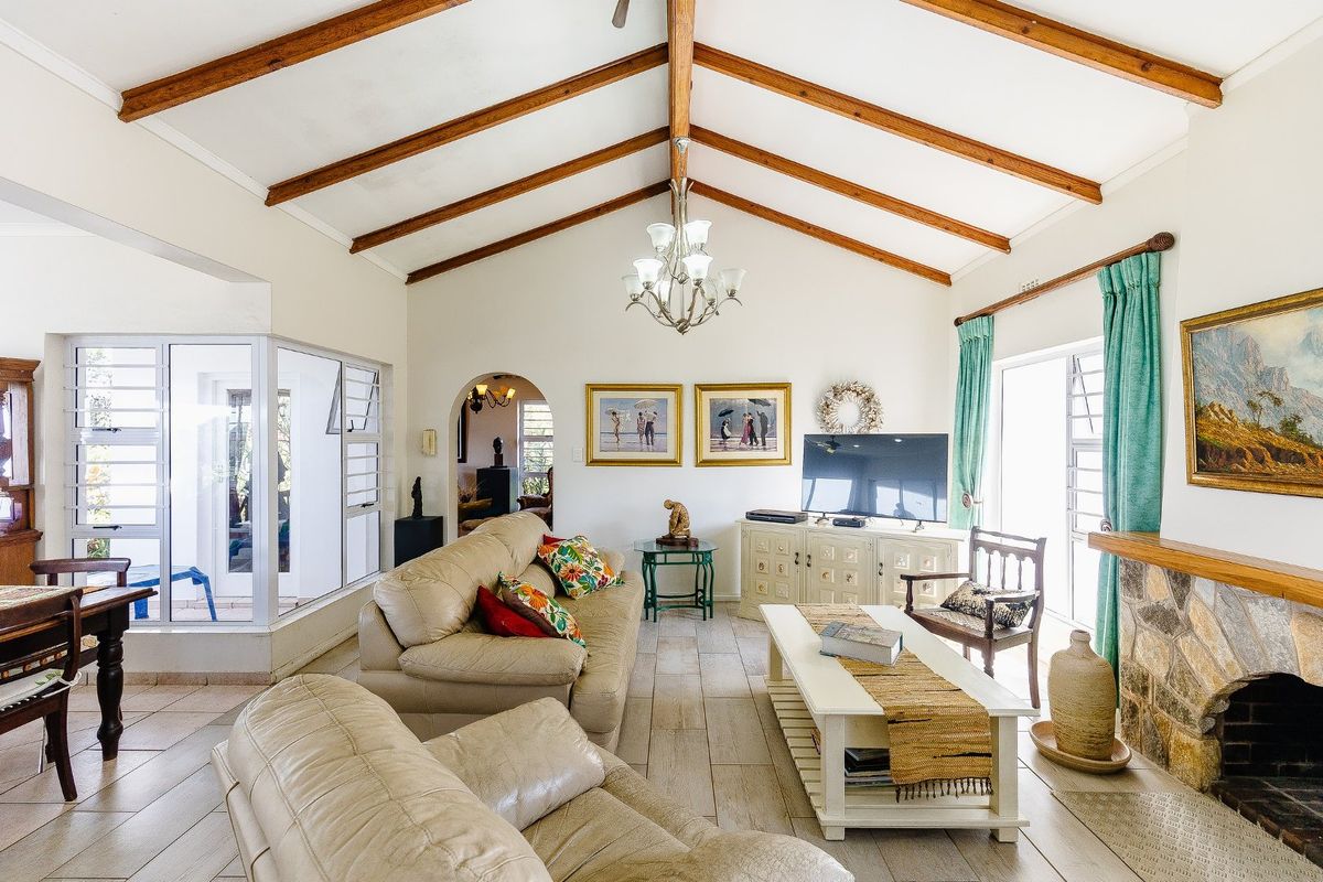Spacious living room featuring a vaulted ceiling with exposed timber beams, a stone fireplace with a timber mantel, and large windows providing natural light.