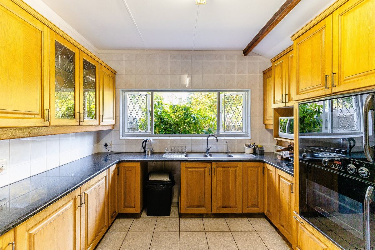 A functional kitchen featuring warm wooden cabinetry, granite countertops, a double bowl sink, and a built-in oven with a tiled backsplash.
