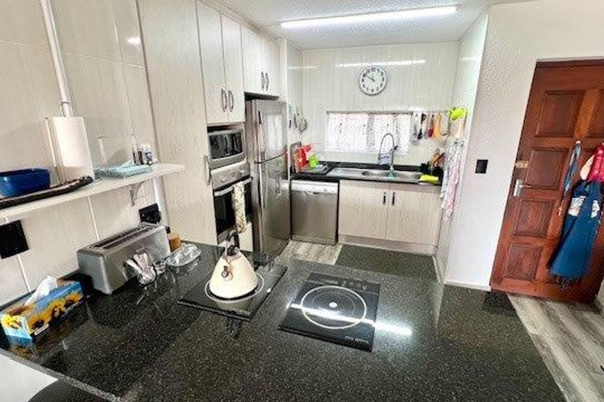 A functional kitchen featuring granite countertops, built-in oven and microwave, induction hob, and ample cabinetry with a tiled backsplash.