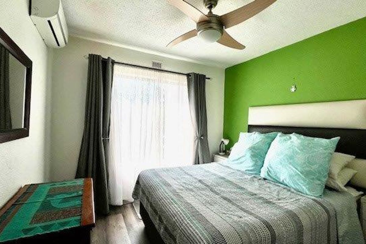 A bedroom featuring a ceiling fan, split-system air conditioning unit, and laminate flooring with a large window providing natural light.