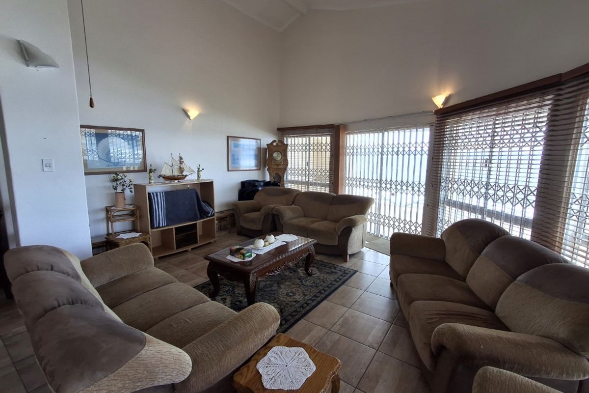 Spacious living room featuring vaulted ceilings, tiled flooring, and large sliding glass doors with security gates leading to an outdoor area.