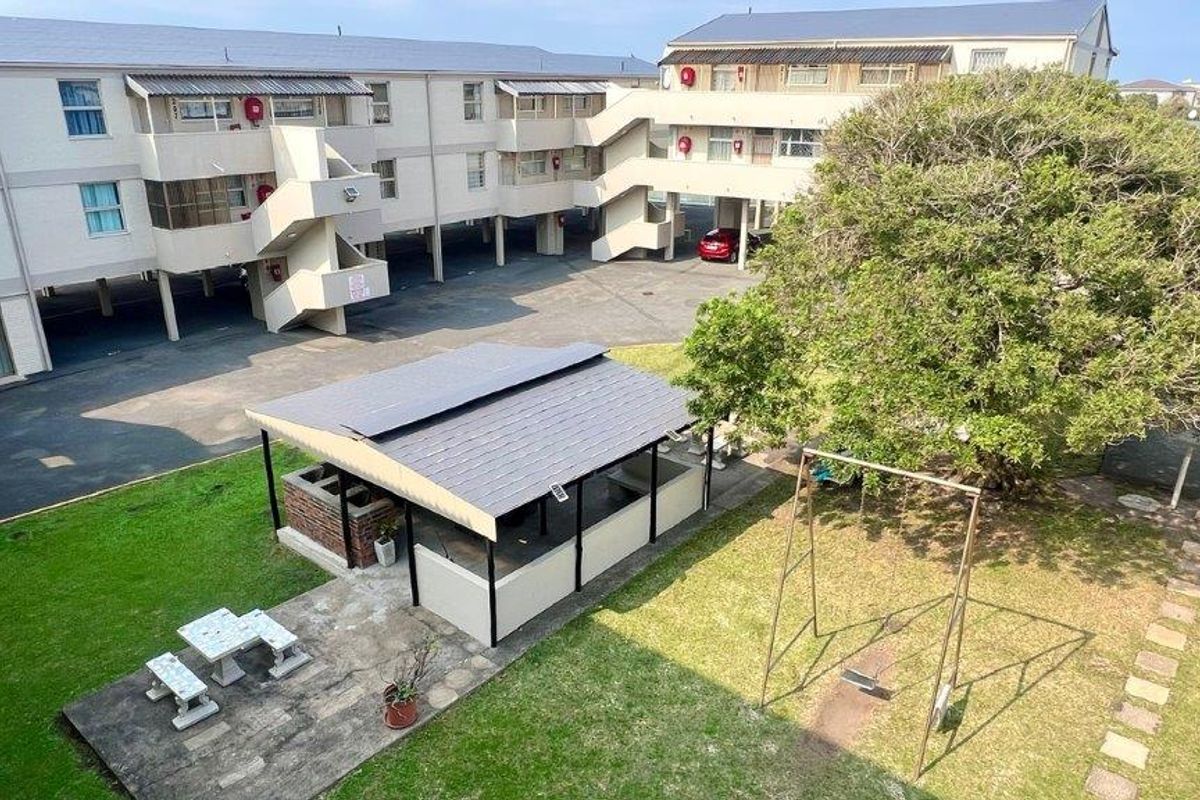 Aerial view of the apartment complex rear courtyard featuring a communal braai area, paved walkways, landscaped garden, and covered parking bays.