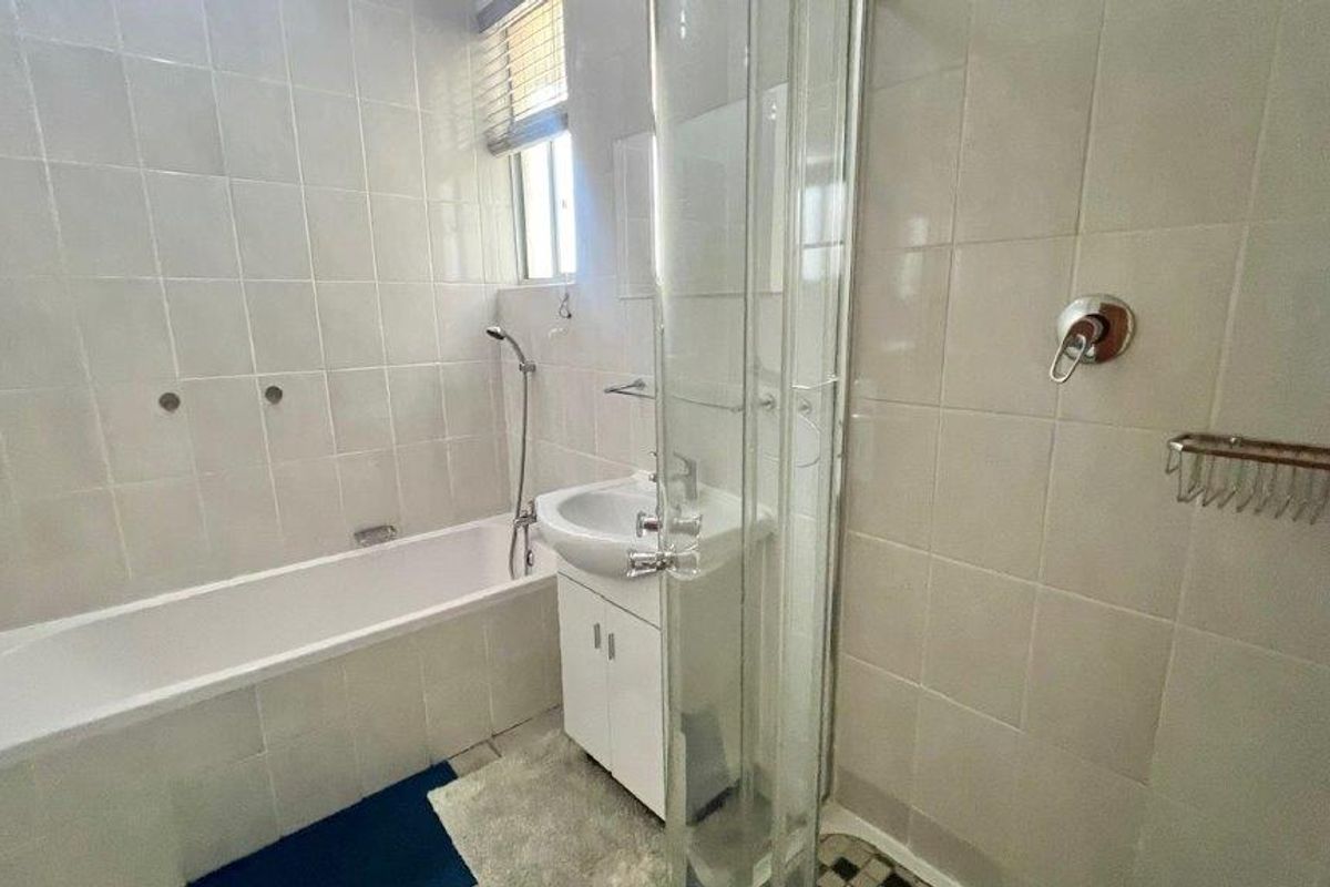 A functional bathroom featuring a built-in bathtub, separate shower enclosure, and a vanity basin with tiled wall finishes.
