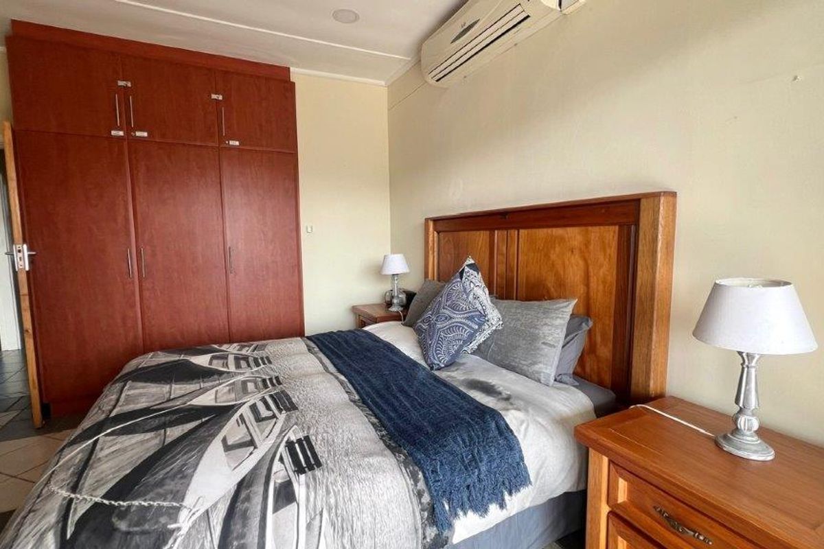 A bedroom featuring built-in wooden cupboards, a wall-mounted air conditioning unit, and tiled flooring.