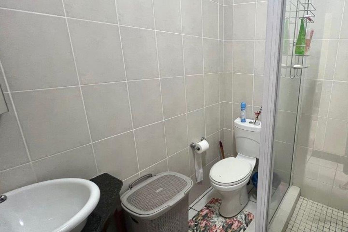 A functional bathroom featuring a vessel sink on a granite vanity, a toilet, and a glass-enclosed shower with neutral wall and floor tiling.