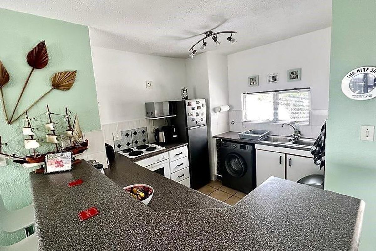 Compact kitchen featuring laminate countertops, built-in oven, electric hob, and a stainless steel sink with tiled backsplash.