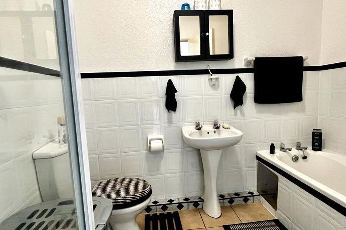 A functional bathroom featuring a pedestal sink, bathtub, separate shower enclosure, and wall-mounted storage cabinet with classic tiled finishes.