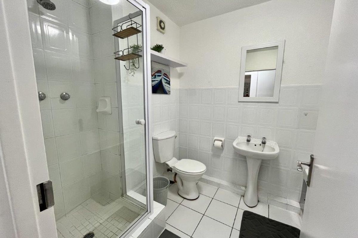 A functional bathroom featuring a glass-enclosed shower, pedestal sink, and toilet with white tiled finishes throughout.